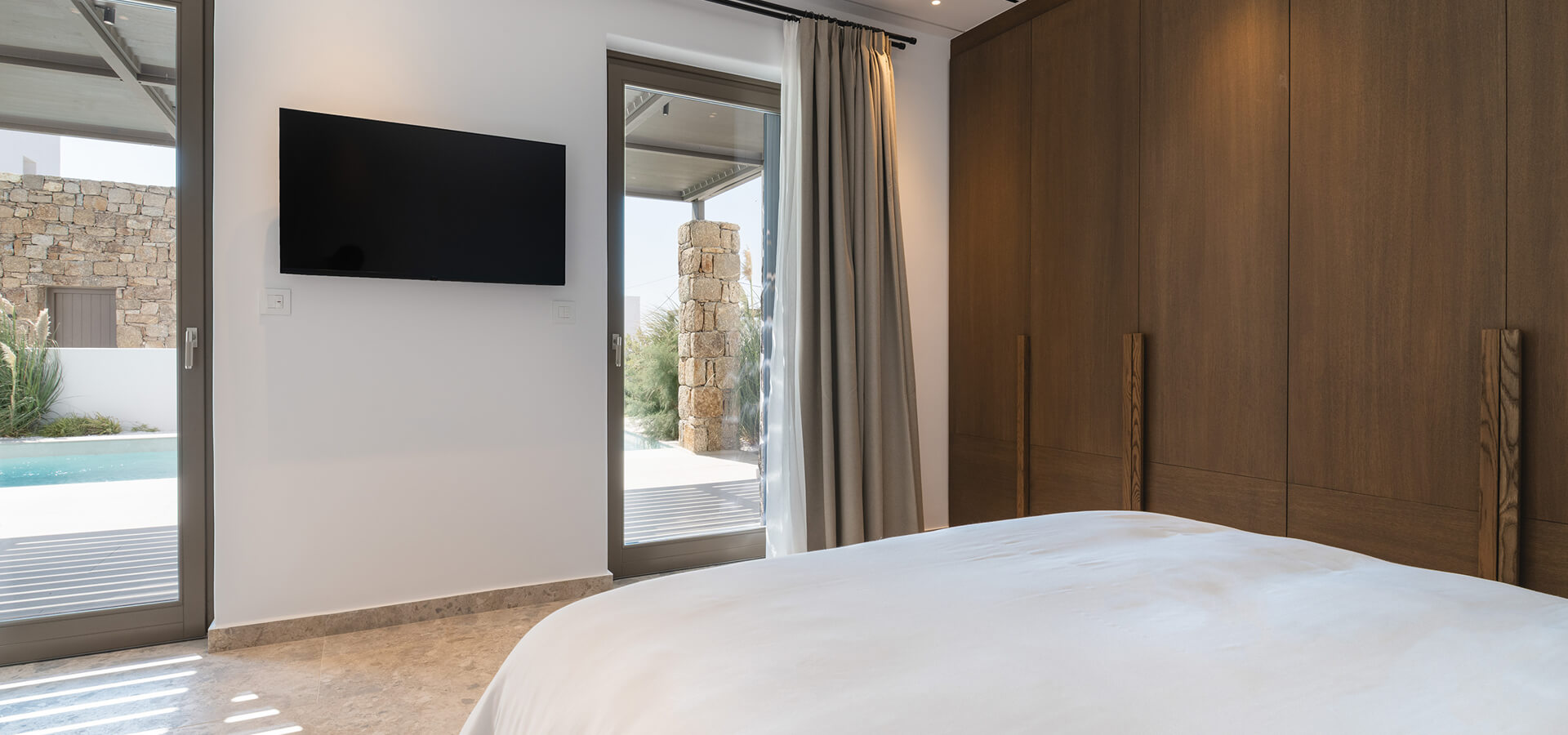 Spacious bedroom with a wall-mounted TV and pool view