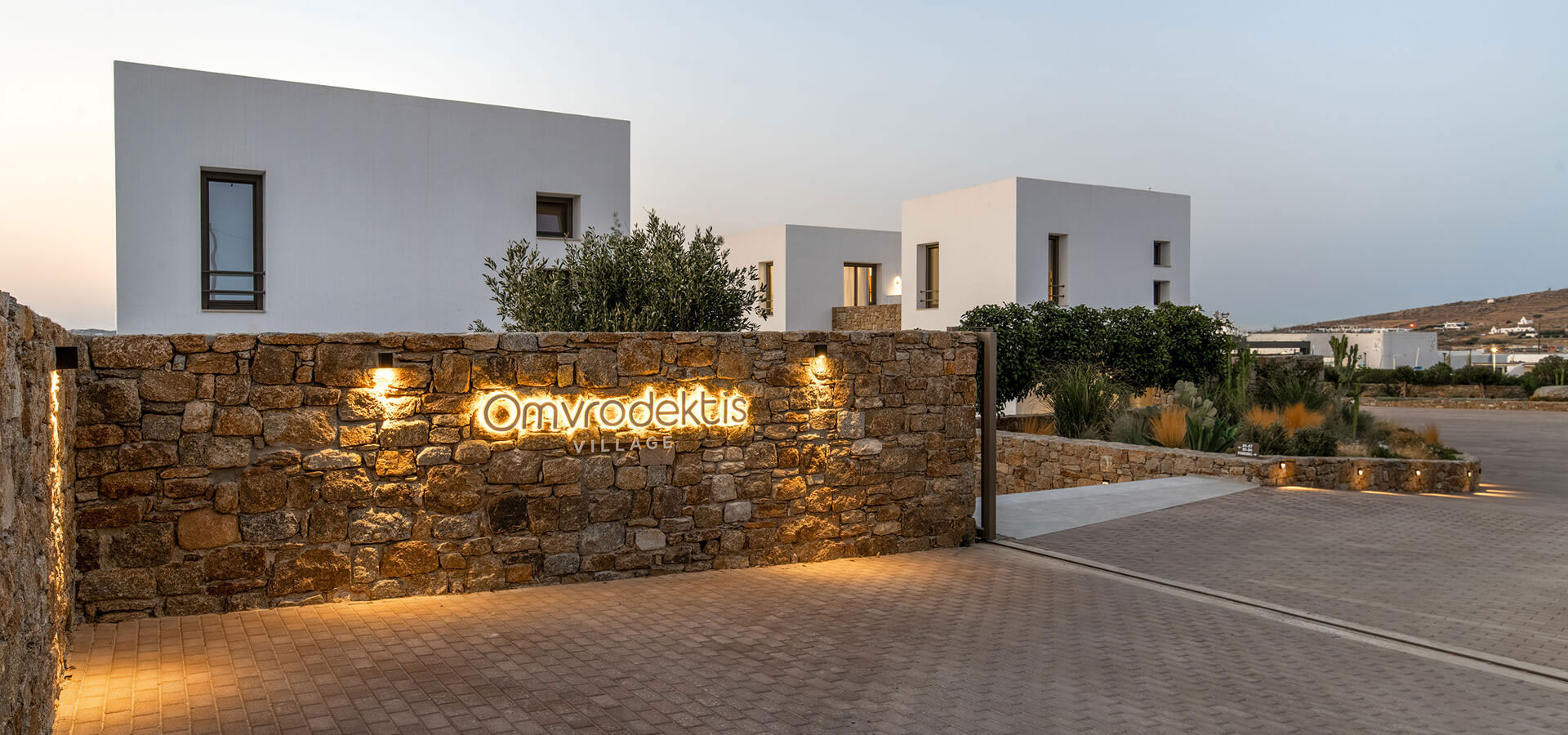 Illuminated Omvrodektis Village sign on a stone wall at the entrance of the Village